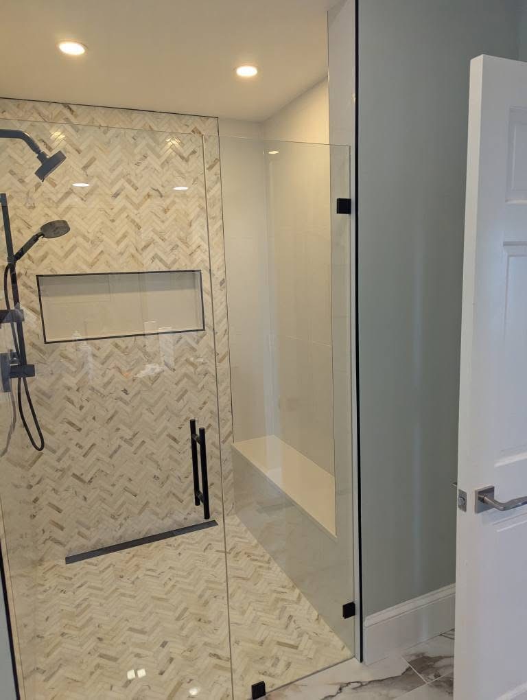 Custom walk-in shower with herringbone marble tile, glass panel, and matte black fixtures in Southern Maine