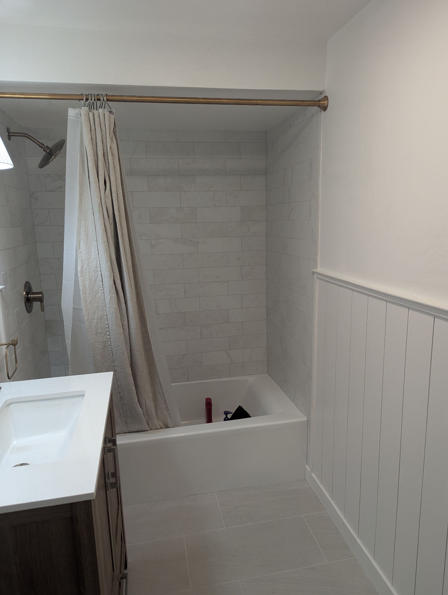 New marble-look subway tile tub surround with brass fixtures and shiplap wainscoting in Portland, Maine