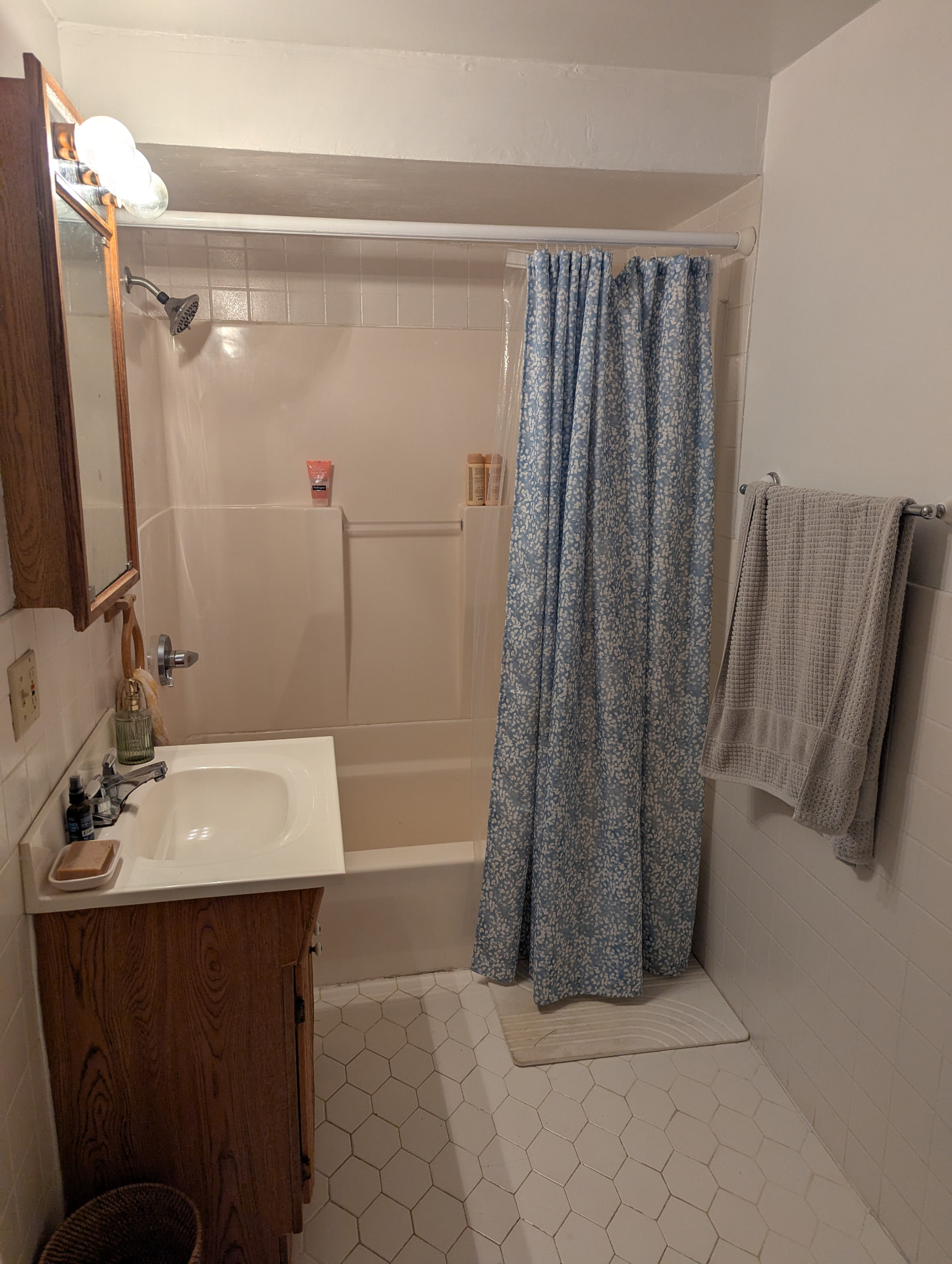 Outdated tub with cream surround and blue shower curtain before remodel in Portland, Maine