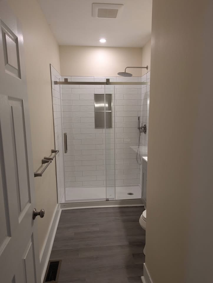 Bathroom shower remodel with white subway tile, sliding glass doors, and luxury vinyl plank flooring in Portland, Maine