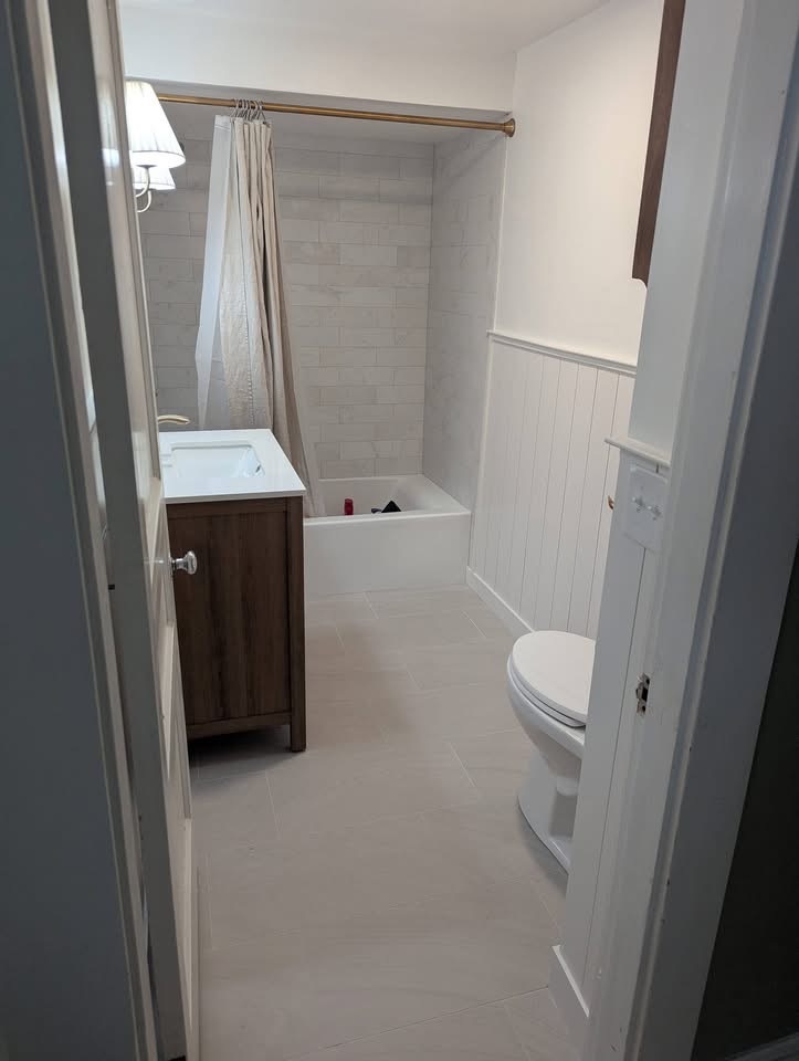Finished bathroom with tiled tub surround, wood vanity, and beadboard wainscoting after remodel in Portland, Maine