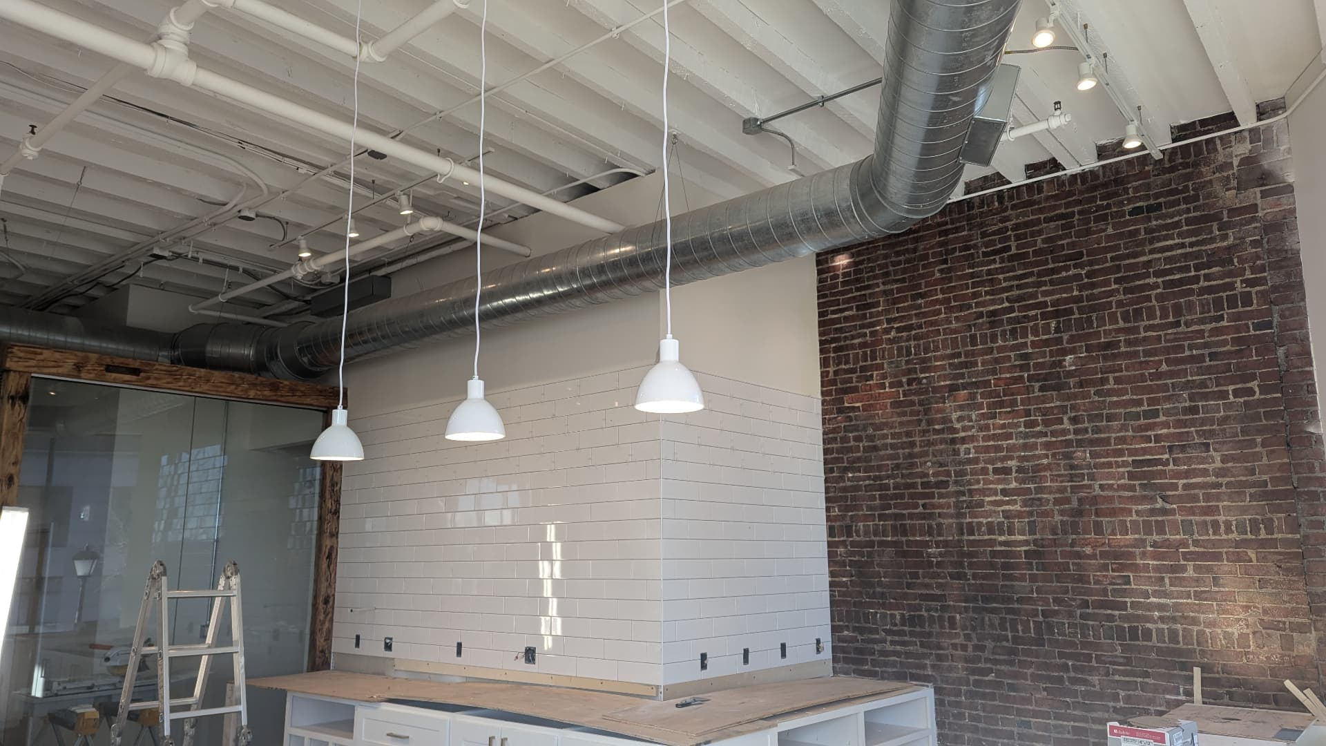 Finished white subway tile wall with white pendant lights beside exposed brick in Portland, Maine