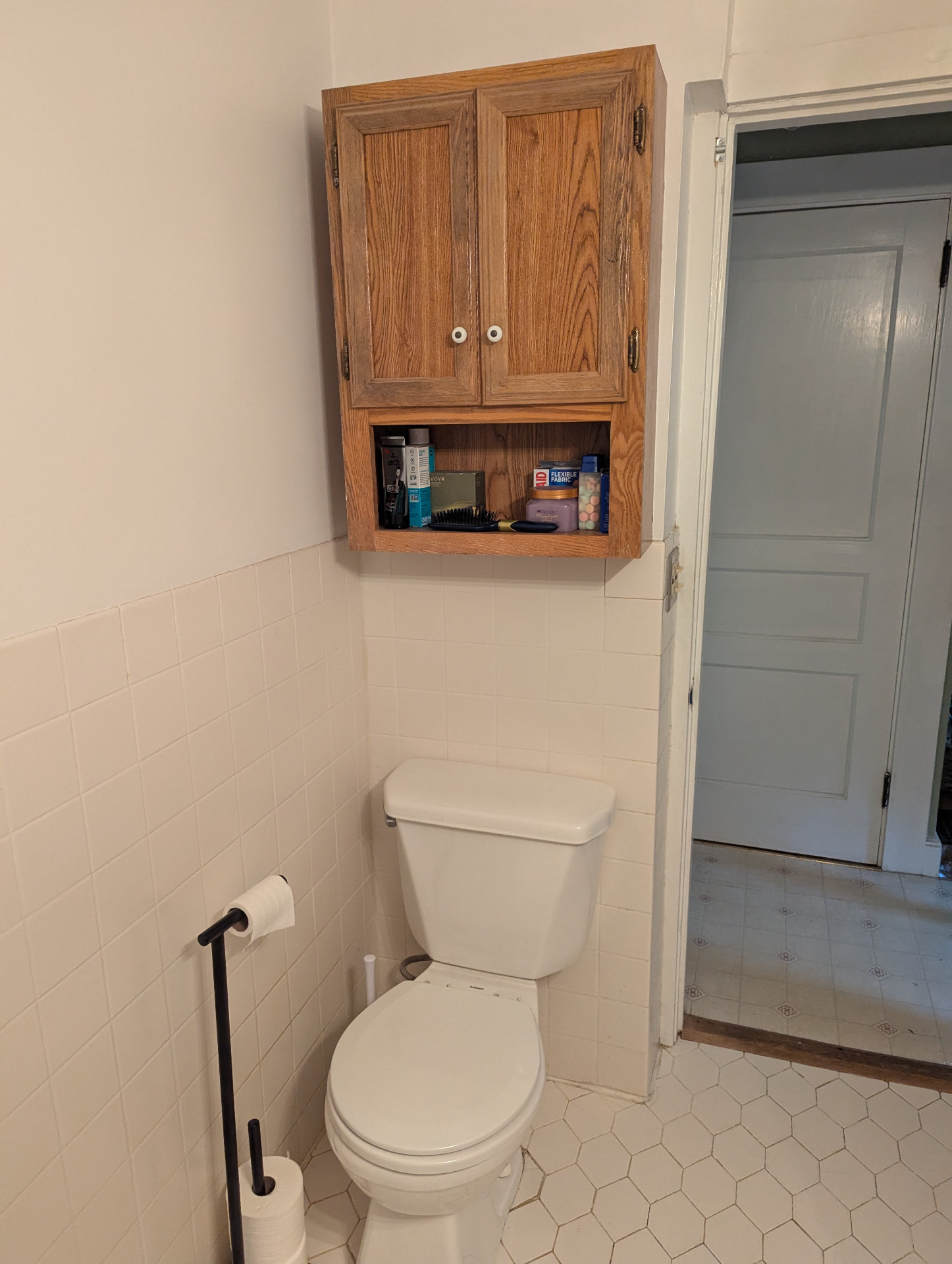 Toilet nook with cream tile and oak wall cabinet before remodel in Portland, Maine