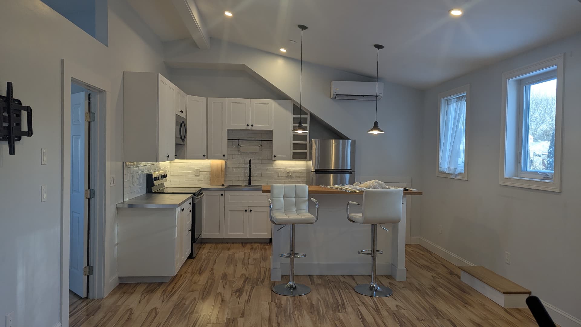 Finished kitchen with white shaker cabinets, subway tile, butcher block island, and pendant lights under a vaulted ceiling in Portland, Maine