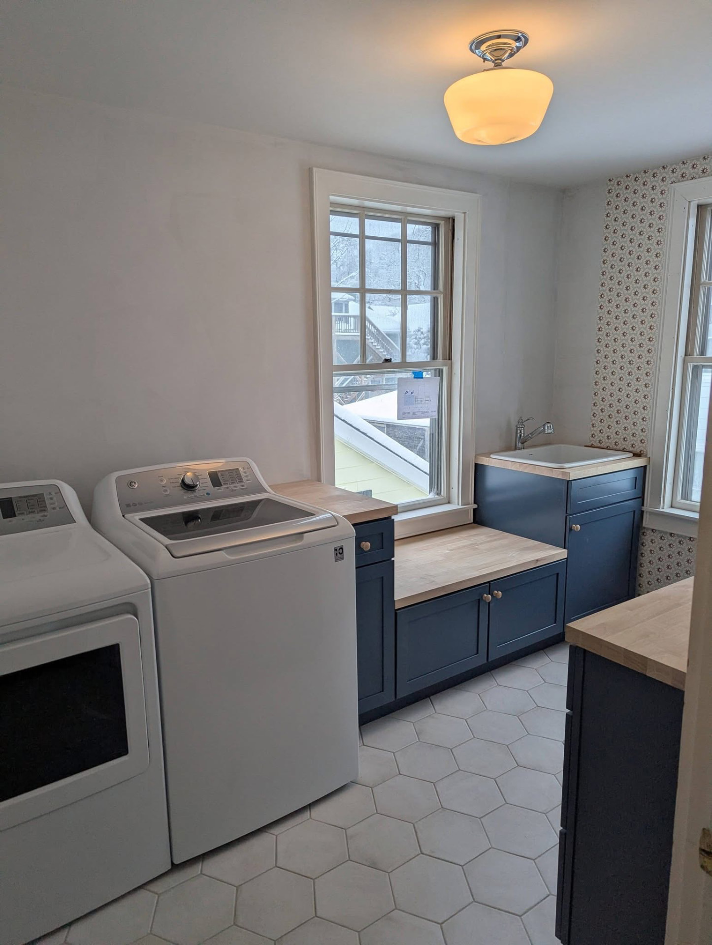 Finished laundry room with navy cabinets, butcher block counters, and hexagon tile floor in Portland, Maine